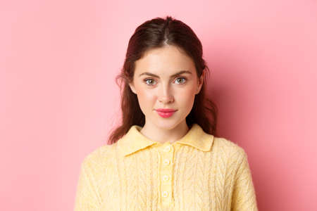 Close up of young glamour girl with cute make up, looking determined at camera, smiling, standing against pink backgroundの写真素材