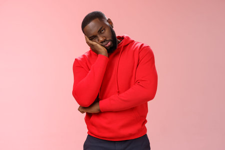 Bored young 25s black guy in red hoodie facepalm lean head hand look indifferent sleepy attend...