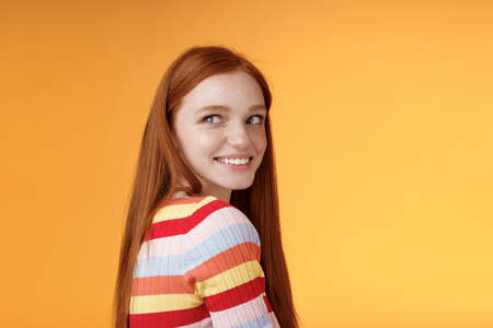 Tender romantic carefree european redhead girlfriend turning behind look left amused smiling pleased coquettish gaze standing orange background flirty romantic mood wanna receive date invitationの写真素材