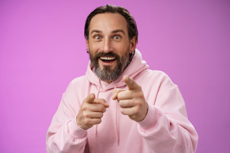 Thrilled energized charismatic happy lucky adult handsome bearded man pointing camera smiling widen...