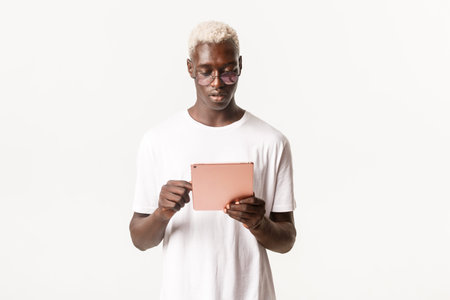 Portrait of handsome and stylish serious african-american man in glasses, looking at digital tablet,...