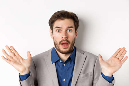 Surprised business man in suit spread hands sideways, looking confused and startled, white backgroundの写真素材