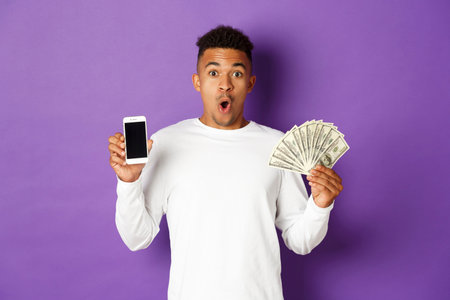 Portrait of handsome african-american man in white sweatshirt, showing money and mobile phone...