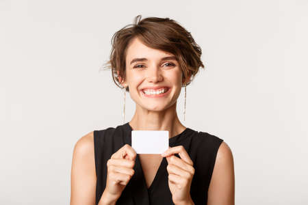 Close-up of happy smiling woman showing her credit card, standing over white backgroundの写真素材