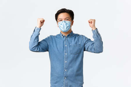 Covid-19, preventing virus, and social distancing at workplace concept. Successful winning asian businessman encourage good team spirit, raising hands up in rejoice, wearing medical maskの写真素材