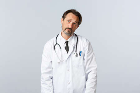 Covid-19, coronavirus outbreak, healthcare workers and pandemic concept. Reluctant uneasy, gloomy doctor sighing and looking up dreamy, imaging want go vacation, have night shiftの写真素材