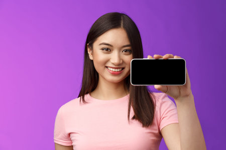 Close-up joyful cute asian woman hold smartphone horizontal, show phone screen, introduce awesome...