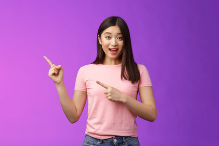Enthusiastic surprised cute asian young girl showing promo lively grinning and telling about hot...