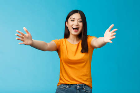 Come closer let me hug you. Cheerful lovely asian brunette girl stretch hands forward wanna cuddle, embracing friend smiling broadly inviting dear guests welcoming, stand blue backgroundの写真素材