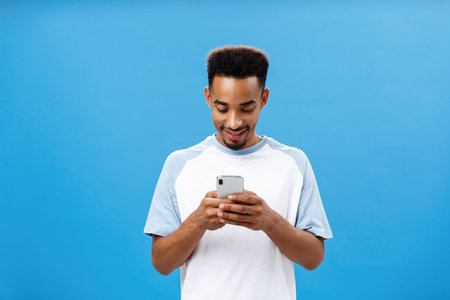 Dark-skinned guy texting with awesome girl via dating app holding smartphone looking in cellphone...