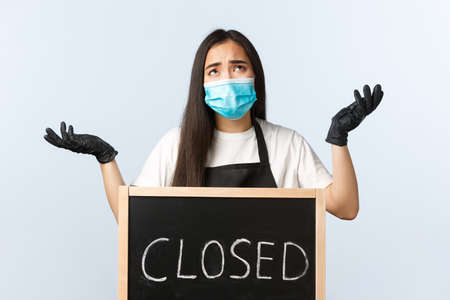 Distressed and sad asian female cafe owner, coffee shop staff complaining on virus lockdown near closed signの写真素材