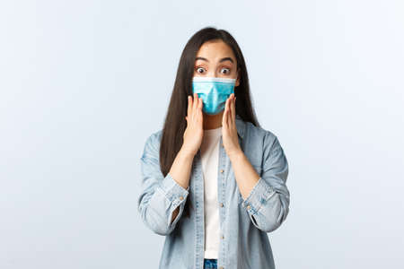 Social distancing lifestyle pandemic everyday life and leisure concept. Surprised astonished asian girl looking impressed, wear medical mask, react to wonderful news, say wowの写真素材