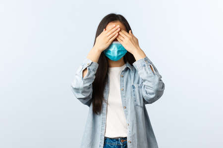 Cute asian girl in medical mask and casual outfit close eyes with hands, playing hide-n-seek or anticipating surpriseの写真素材