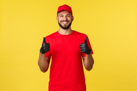 Express mail delivery, package transfer and logistics concept. Satisfied bearded handsome courier, deliver fast and safe parcel, show thumbs-up, wearing uniform and protective glovesの写真素材