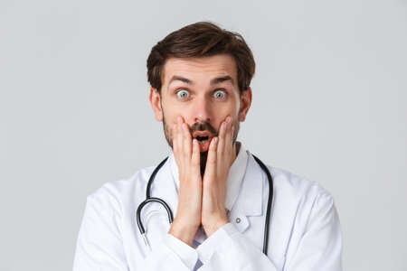 Hospital, healthcare workers, covid-19 treatment concept. Close-up shot of amazed, speechless doctor, gasping open mouth and staring astonished, hold hands near mouth impressed over big newsの写真素材