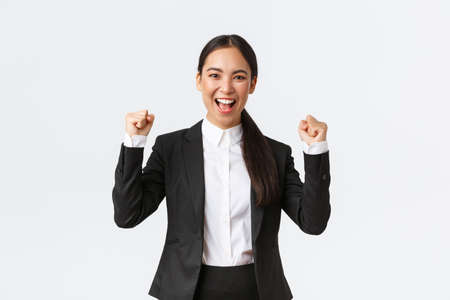Successful winning female entrepreneur in black suit, fist pump and shouting yes excited, celebrating victory. Businesswoman triumphing over big achievement over white backgroundの写真素材