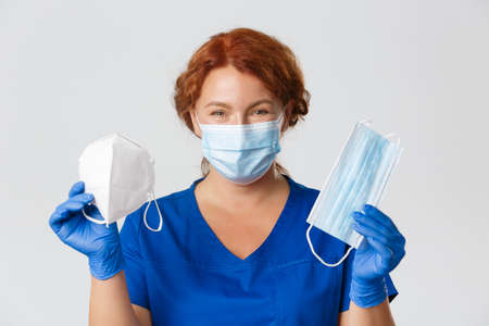 Medical workers, covid-19 pandemic, coronavirus concept. Close-up of smiling female doctor, physician recommend protective equipment, showing face mask and respirator, grey backgroundの写真素材