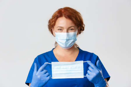 Medical workers,  pandemic, virus concept. Close-up of smiling friendly-looking female doctor, physician explain how to wear face mask, holding it with rubber glovesの写真素材