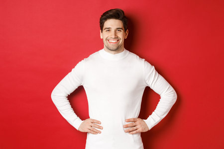 Portrait of handsome man with bristle, wearing white sweater, smiling and looking confident,...