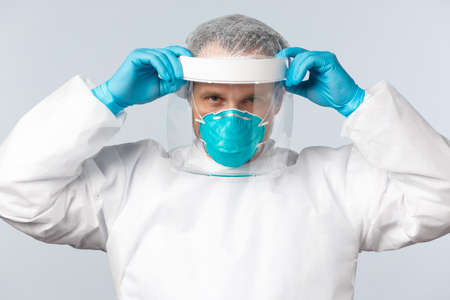 virus, healthcare workers and vaccination concept. Determined professional doctor in personal protective equipment, put on face shield and respirator while working with virus diseaseの写真素材
