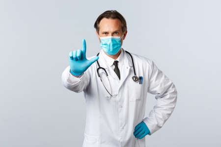 preventing virus, healthcare workers and vaccination concept. Serious confident doctor in medical mask and gloves, shaking finger scolding, prohibit or warn patients with virusの写真素材