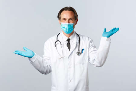 preventing virus, healthcare workers and vaccination concept. Smiling handsome doctor give two variants, wear medical mask and gloves, showing left and right products, white backgroundの写真素材
