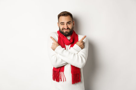 Winter holidays and shopping concept. Bearded man looking indecisive, asking for advice with choice, picking christmas gifts, pointing sideways, standing over white backgroundの写真素材