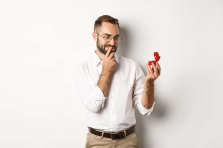 Happy man looking thoughtful at wedding ring in box, thinking about marriage proposalの写真素材