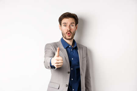 Image of handsome businessman in suit showing thumb up with excited face, standing on white backgroundの写真素材