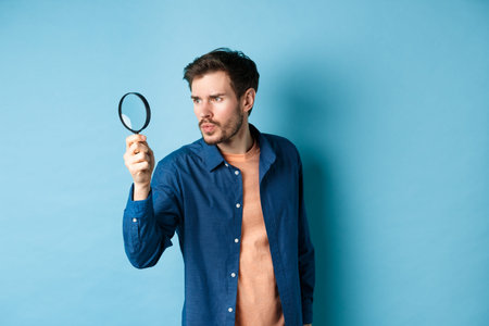 Serious man investigating or searching for something, look through magnifying glass like detective,...