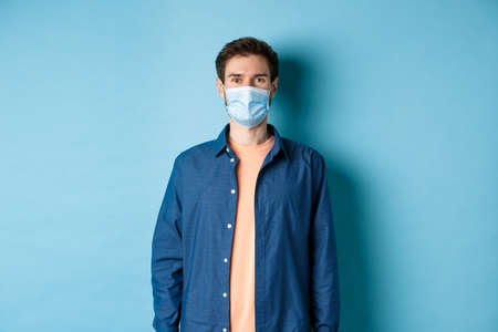 Covid-19 and healthcare concept. Smiling young man in medical mask looking healthy and happy, standing on blue backgroundの写真素材
