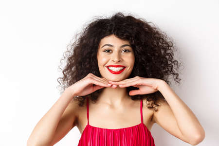 Beauty and makeup. Pretty lady with curly hair, red lips and white teeth, smiling and showing perfect face, standing on white backgroundの写真素材