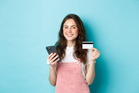 Young smiling woman making online payment, shop online with credit card and smartphone in hands,...