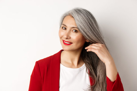 Beauty and haircare concept. Close up of elegant asian senior woman showing shiny and healthy grey...