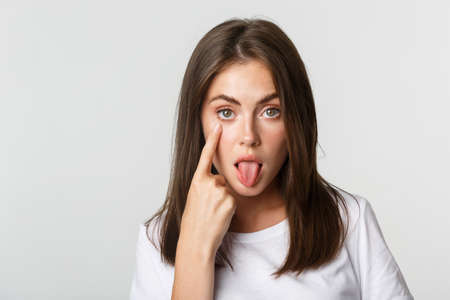 Close-up of silly attractive young girl showing tongue and pulling eyelid, watching youの写真素材