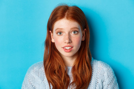 Headshot of cute redhead girl with freckles, looking hopeful and innocent at camera, standing over...