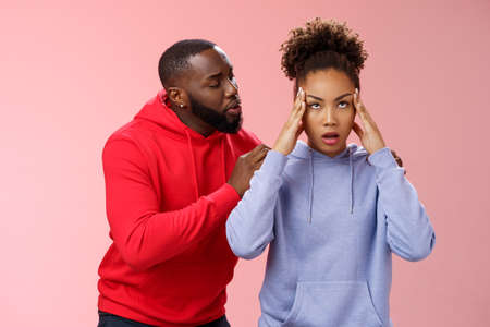 Man apologizing girlfriend behind back touching shoulder comforting girl feel pressured irritated fed up lying hear boyfriend sorry arguing standing bothered pink background, couple fightingの写真素材