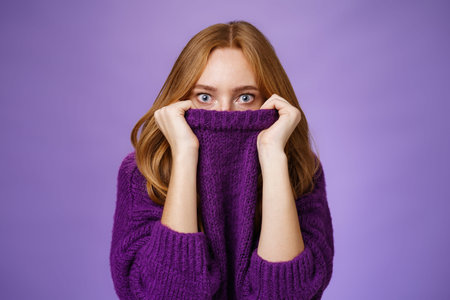 Redhead girl scared winter is comming hiding in collar of warm sweater popping eyes shocked and...