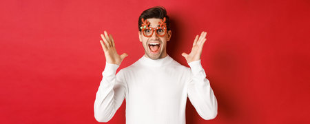 Close-up of surprised handsome guy in white sweater and party glasses, hear amazing christmas promo...