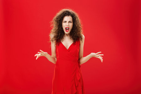 Dissatisfied angry and pissed attractive curly-haired female in stylish red dress arguing and frowning being bothered and in fury while fighting with boyfriend being shocked dinner ruinedの写真素材