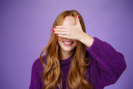 Happiness, emotions and anticipation concept. Charming dreamy ginger girlfriend with cute nails covering eyes with raised palm and smiling broadly waiting for surprise or miracle, playing peekabooの写真素材