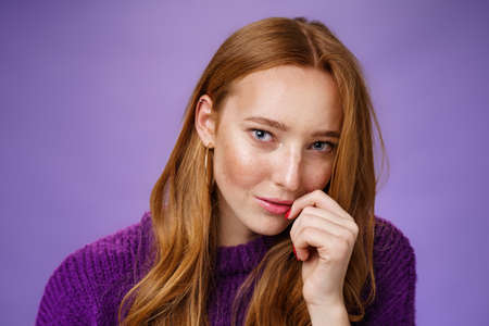 Ginger girl charmes with sensual romantic gaze. Portrait of confident flirting and attractive redhead female tilting head touching lips and looking daring at camera against purple backgroundの写真素材