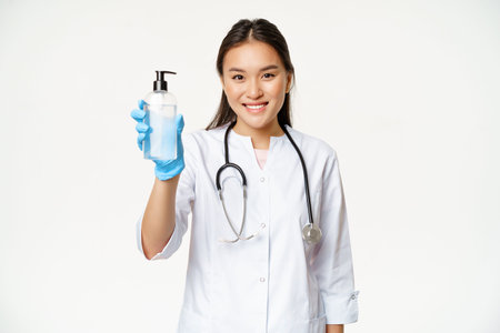 Smiling asian doctor showing hand sanitizer, bottle of antiseptic, wearing sterile rubber gloves and...
