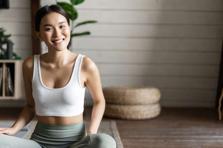 Mindfulness and meditation concept. Young asian woman doing workout at home, yoga meditation in living room on floor mat, getting focusedの写真素材