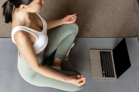 Cropped shot of asian woman meditating in floor mat at home, listening to meditation podcast on laptop, practice yoga online courase, wearing activewearの写真素材