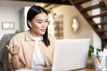 Young asian woman working, talking on video conference, chatting on laptop video messanger, has...