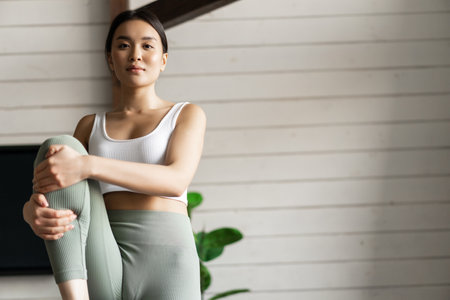 Portrait of asian girl doing workout at home, lifting legs and looking at distance, exercising in living room without fitness gearの写真素材