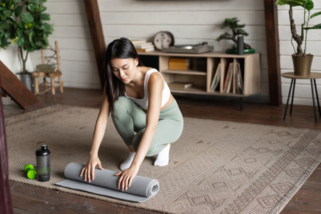 Asian fitness girl finish training,workout at home, rolling floor mat after exercises in living roomの写真素材