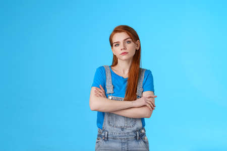 Serious-looking professional bossy redhead female skilfull girl, cross arms confident self-assured pose, look camera no emotions strict determined, aim win, stand blue background encouragedの写真素材