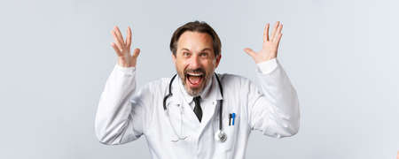 healthcare workers and vaccination concept. Close-up of mad outraged doctor in white coat, raising hands up and shouting furious, being angryの写真素材